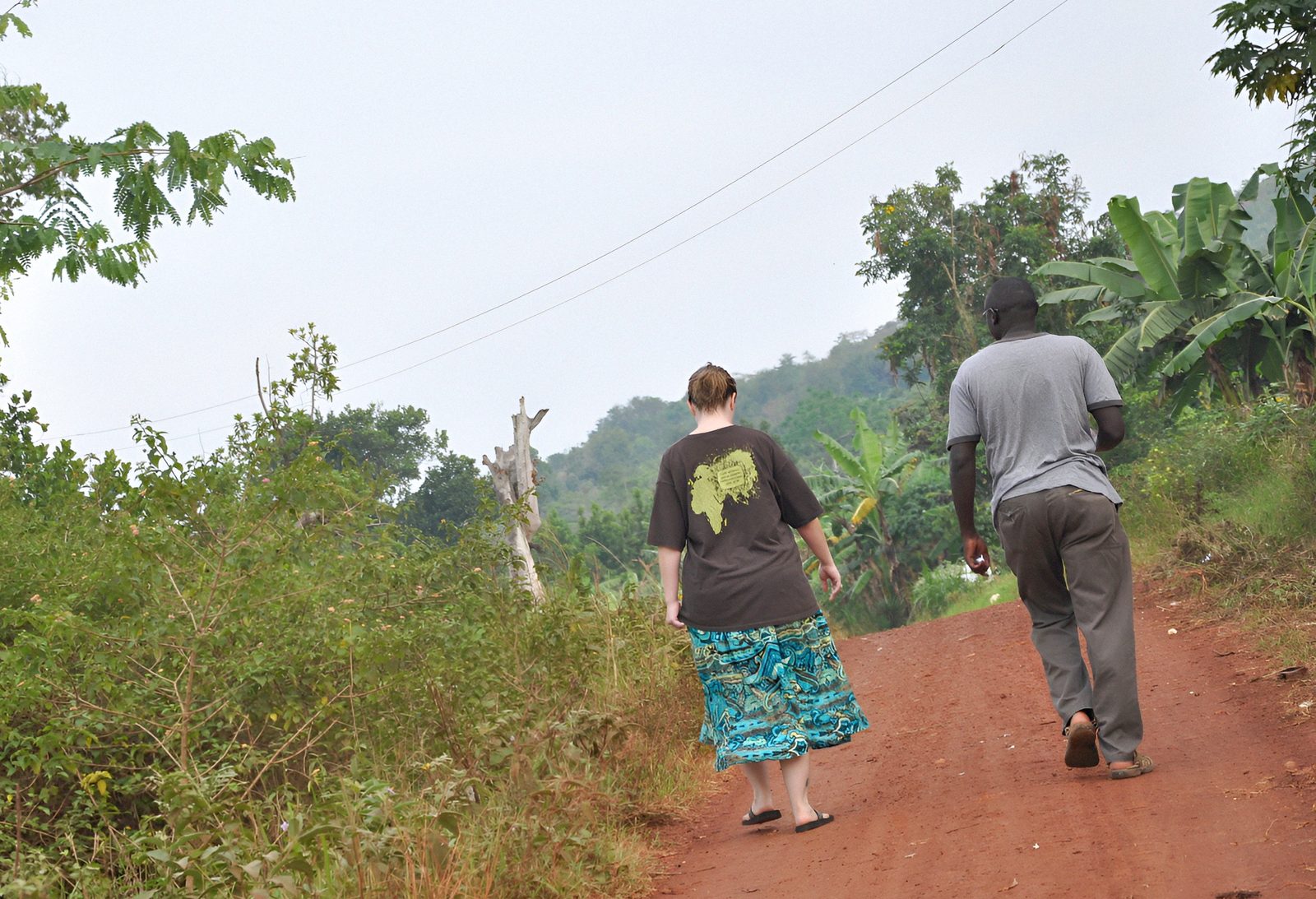 Christie and George Magera walking a red-earth path together in rural Uganda, a visual embodiment of the Luganda word ekubo meaning path